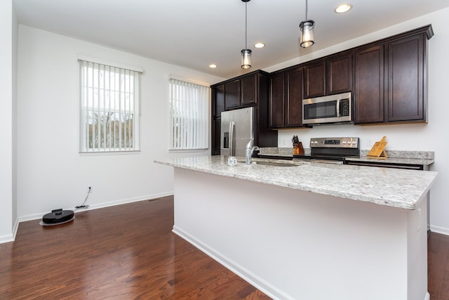 kitchen with a kitchen island with sink, appliances with stainless steel finishes, a sink, and decorative light fixtures