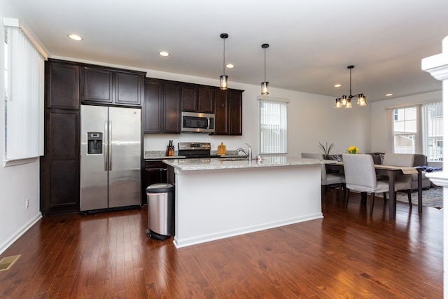 kitchen with a sink, hanging light fixtures, appliances with stainless steel finishes, an island with sink, and dark wood finished floors