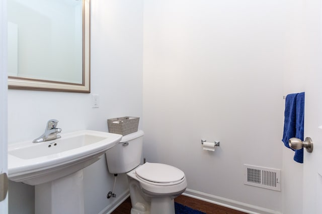 half bathroom with toilet, wood finished floors, a sink, visible vents, and baseboards