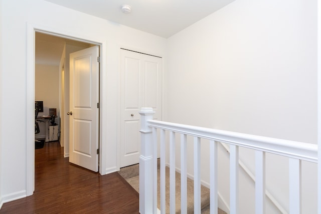 hall with a wainscoted wall, dark wood finished floors, and an upstairs landing