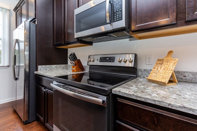 kitchen featuring appliances with stainless steel finishes, light stone counters, dark brown cabinets, and wood finished floors