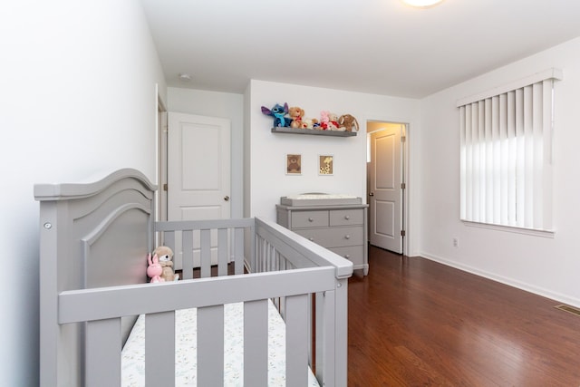 bedroom featuring dark wood-style floors, a nursery area, visible vents, and baseboards