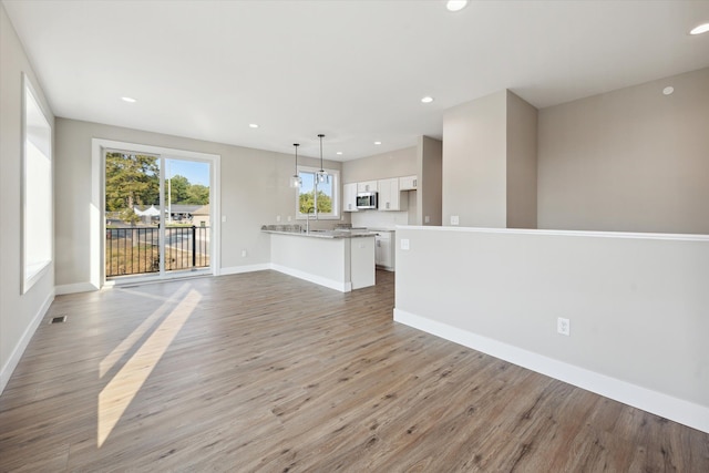 unfurnished living room featuring baseboards, light wood-type flooring, a sink, and recessed lighting