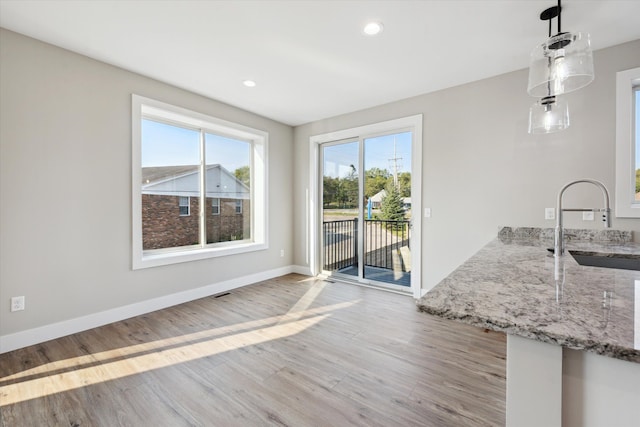 kitchen featuring light stone counters, pendant lighting, light wood finished floors, a sink, and baseboards