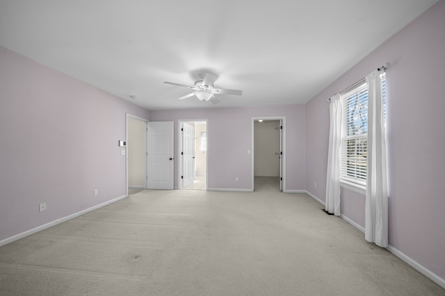 unfurnished bedroom featuring a ceiling fan, baseboards, ensuite bath, a spacious closet, and light colored carpet