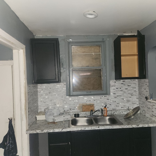 kitchen with dark cabinets, arched walkways, backsplash, and a sink