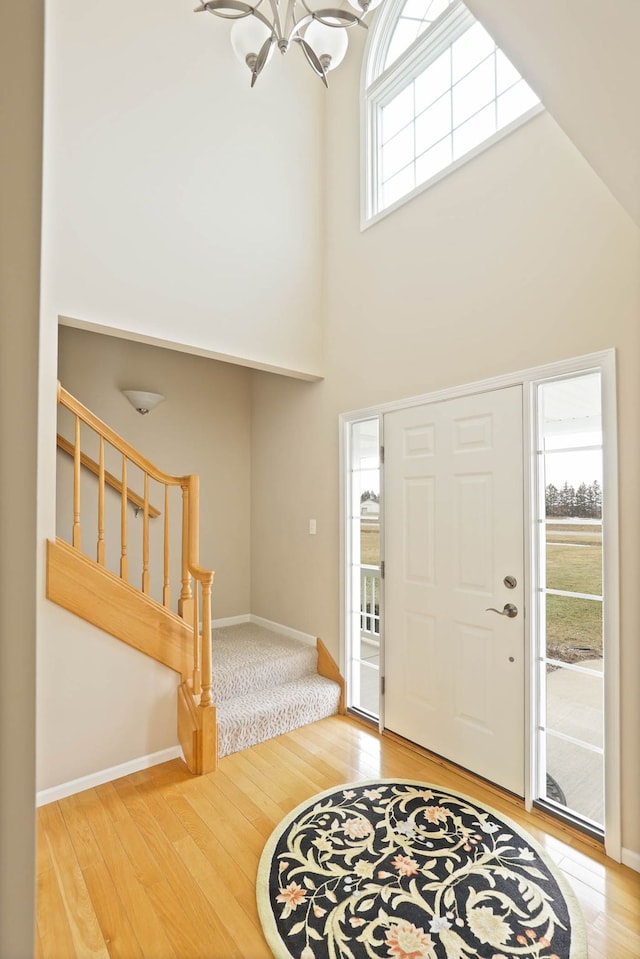 entryway featuring baseboards, stairway, hardwood / wood-style floors, an inviting chandelier, and a high ceiling