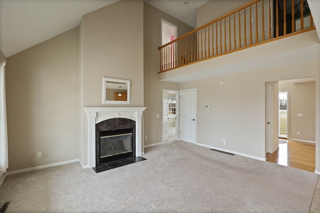 unfurnished living room featuring high vaulted ceiling, a tile fireplace, baseboards, and carpet