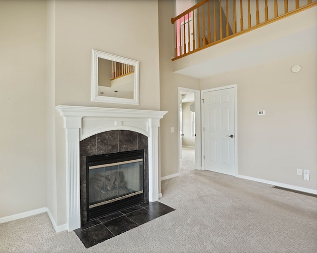 unfurnished living room featuring carpet floors, a high ceiling, baseboards, and a tile fireplace