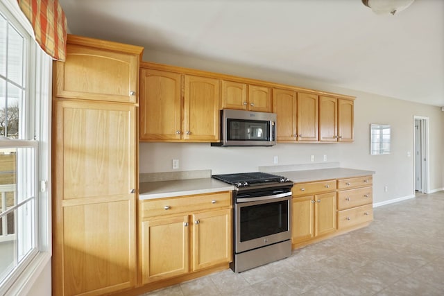 kitchen with light brown cabinets, stainless steel appliances, light countertops, and baseboards