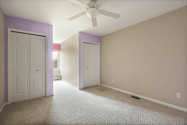 unfurnished bedroom with a ceiling fan, multiple closets, visible vents, baseboards, and carpet