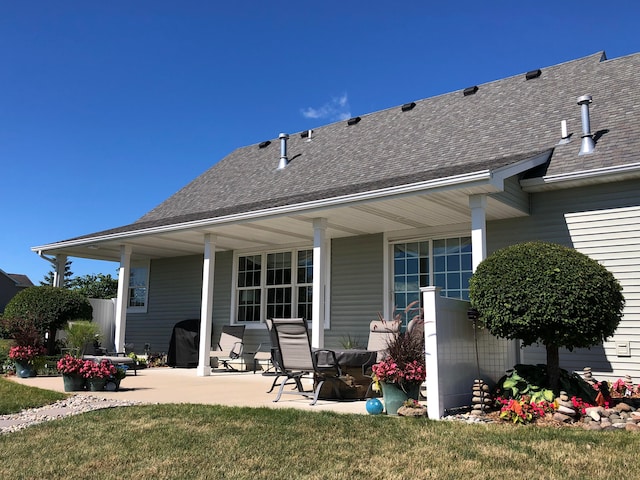 back of property with a patio, roof with shingles, and a lawn