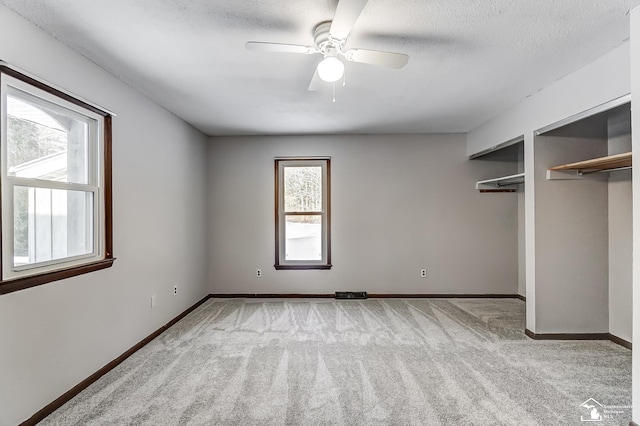 unfurnished bedroom featuring ceiling fan, a textured ceiling, light carpet, multiple closets, and baseboards