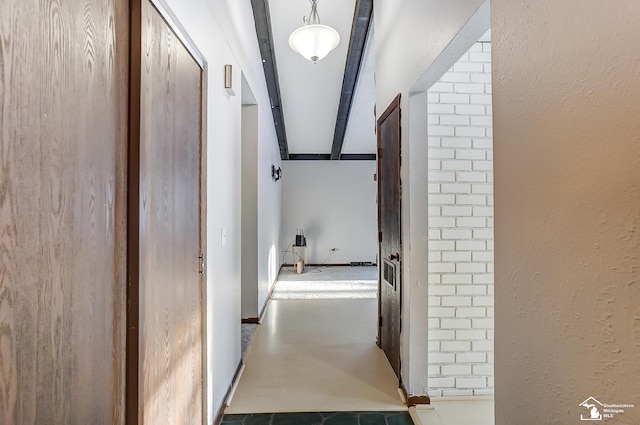 corridor featuring concrete flooring, a textured wall, and beam ceiling