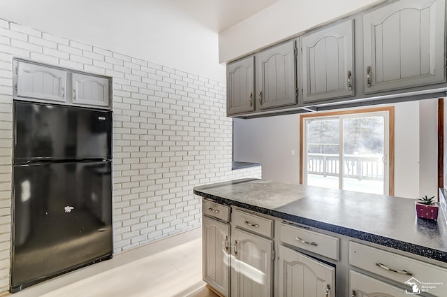 kitchen with dark countertops, brick wall, gray cabinets, and freestanding refrigerator