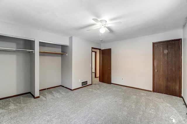 unfurnished bedroom featuring visible vents, baseboards, light colored carpet, ceiling fan, and two closets