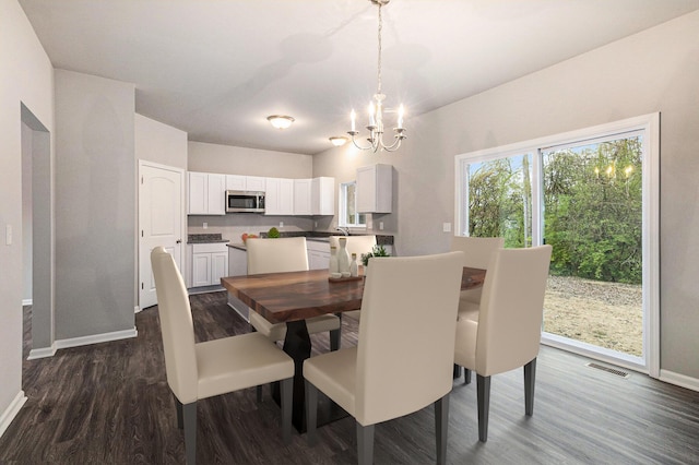 dining area with dark wood-style floors, visible vents, a notable chandelier, and baseboards