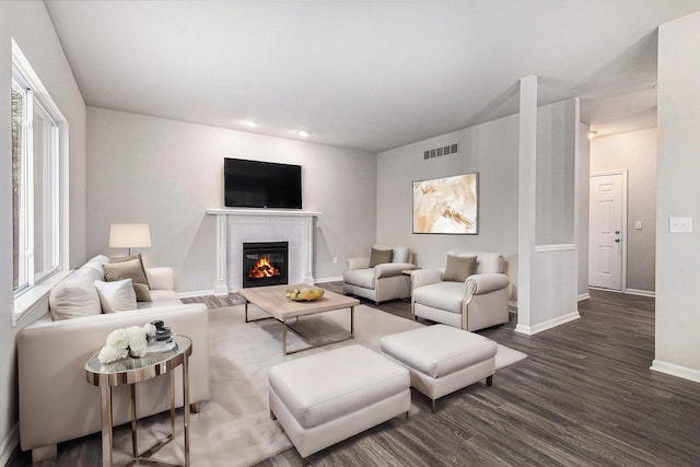 living room featuring a glass covered fireplace, dark wood-style flooring, visible vents, and baseboards