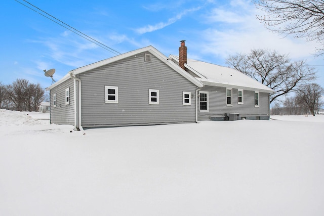 snow covered back of property with central AC and a chimney