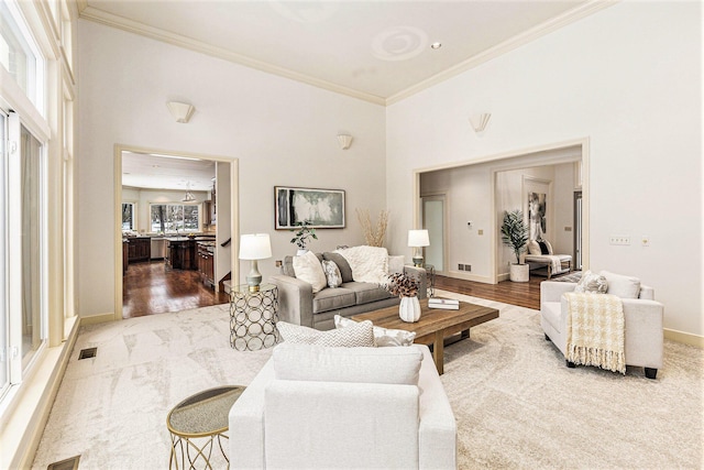 living room featuring baseboards, visible vents, a high ceiling, crown molding, and light wood-type flooring