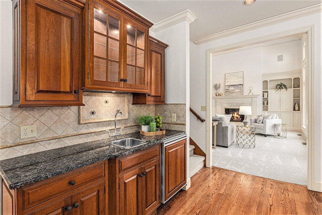 kitchen featuring crown molding, glass insert cabinets, open floor plan, a sink, and dark stone countertops