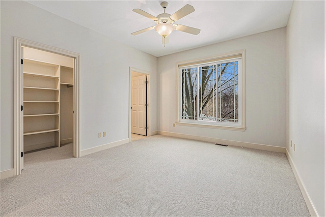 unfurnished bedroom featuring baseboards, visible vents, a ceiling fan, light colored carpet, and a walk in closet