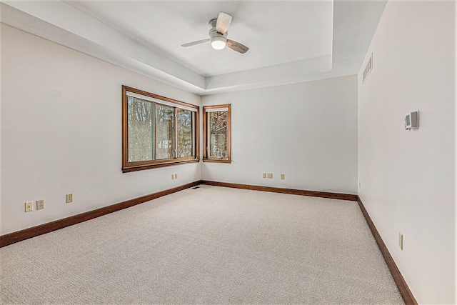 spare room with ceiling fan, visible vents, baseboards, a tray ceiling, and carpet