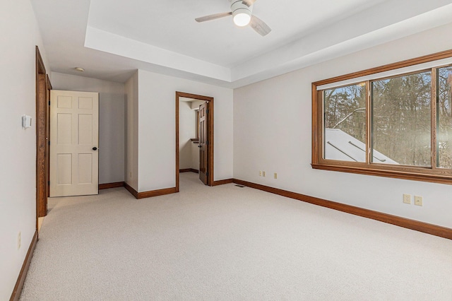 unfurnished bedroom with baseboards, a raised ceiling, a walk in closet, and light colored carpet