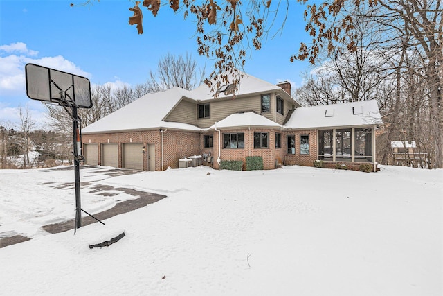 view of front facade featuring an attached garage, central air condition unit, brick siding, a sunroom, and a chimney