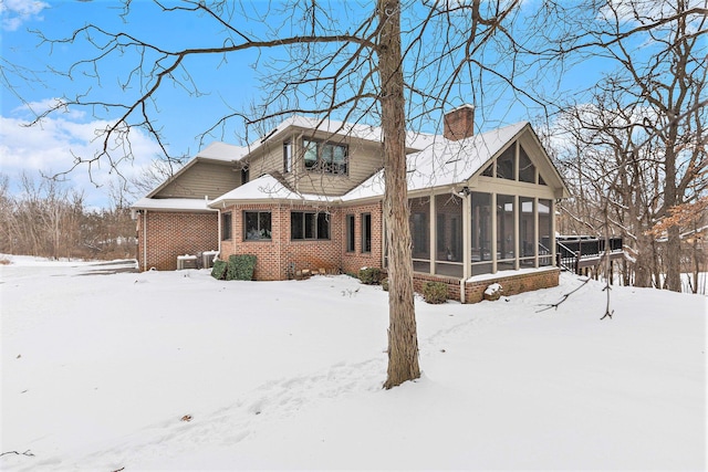 snow covered house featuring a garage, a sunroom, a chimney, and brick siding