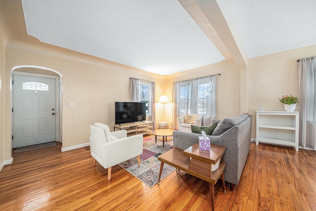 living area featuring arched walkways, baseboards, and wood finished floors