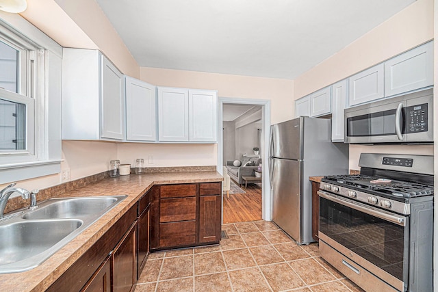 kitchen featuring appliances with stainless steel finishes, light tile patterned flooring, a sink, and white cabinetry