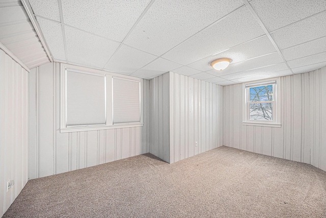 interior space with wood walls, carpet, and a drop ceiling