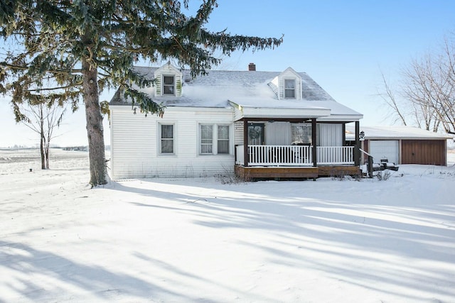 cape cod house featuring covered porch, a detached garage, a chimney, and an outdoor structure