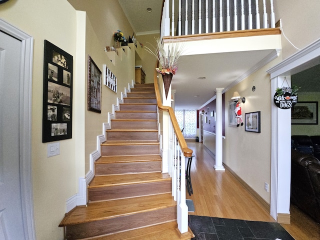 stairway with crown molding, decorative columns, baseboards, and wood finished floors