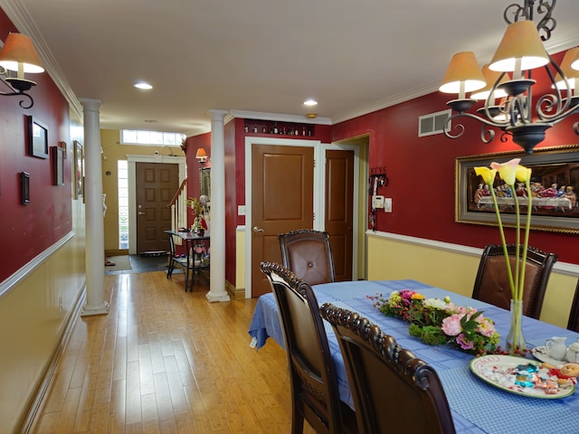 dining room with visible vents, light wood-type flooring, ornate columns, an inviting chandelier, and crown molding