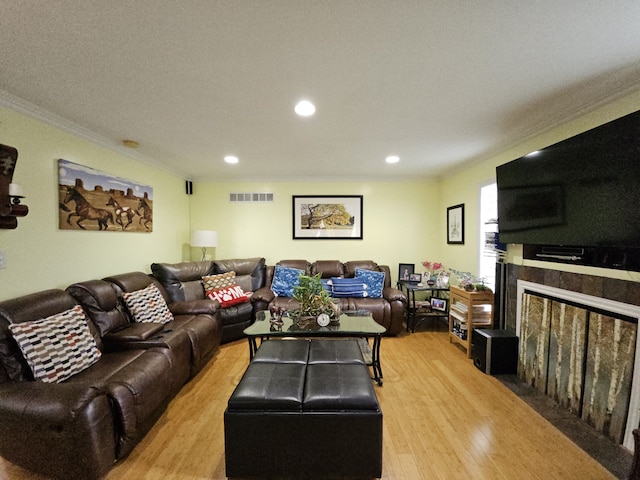 living room featuring crown molding, light wood finished floors, recessed lighting, visible vents, and a fireplace with flush hearth