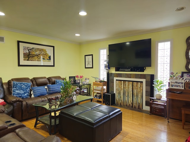 living area featuring light wood-type flooring, visible vents, a fireplace, and ornamental molding