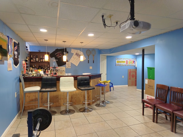 bar featuring a paneled ceiling, light tile patterned flooring, hanging light fixtures, and a bar