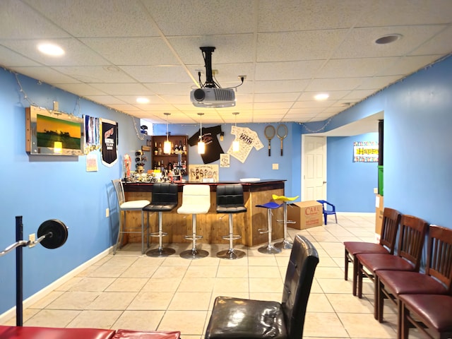 bar with a dry bar, baseboards, tile patterned floors, a paneled ceiling, and pendant lighting