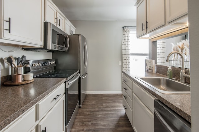 kitchen featuring stainless steel appliances, dark countertops, white cabinets, and a sink