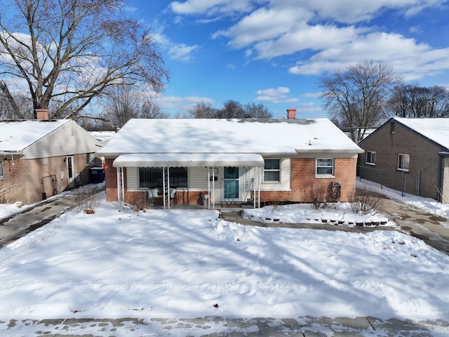 snow covered rear of property with a chimney and brick siding