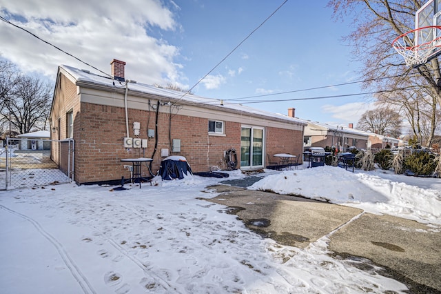 snow covered back of property with a chimney, fence, and brick siding