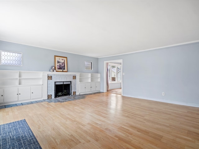 unfurnished living room featuring a brick fireplace, light wood-style flooring, baseboards, and crown molding