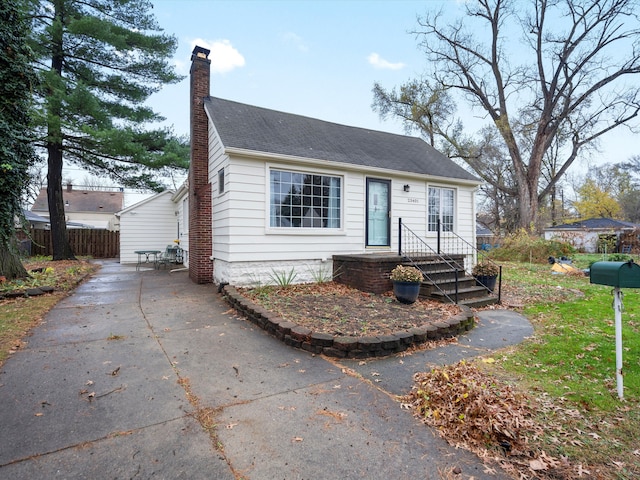 view of front of home featuring driveway, a chimney, and fence