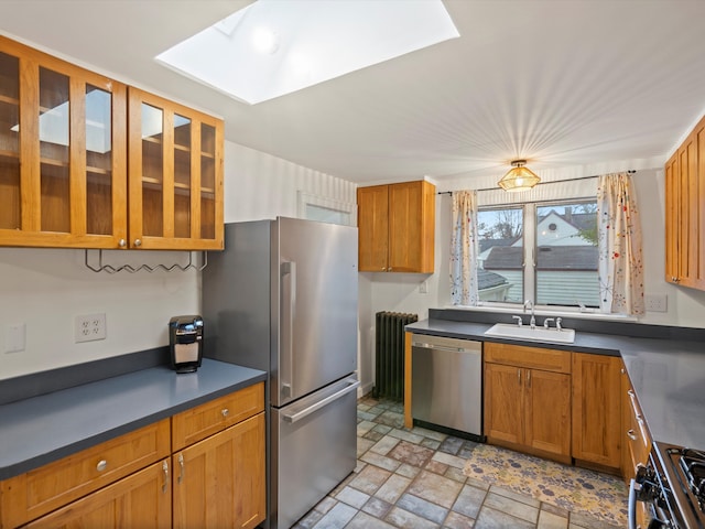 kitchen featuring dark countertops, glass insert cabinets, stone finish flooring, stainless steel appliances, and a sink