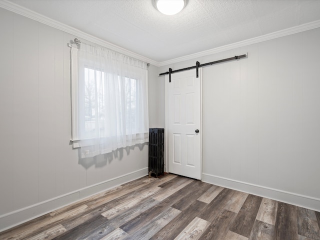 spare room with a barn door, ornamental molding, and wood finished floors