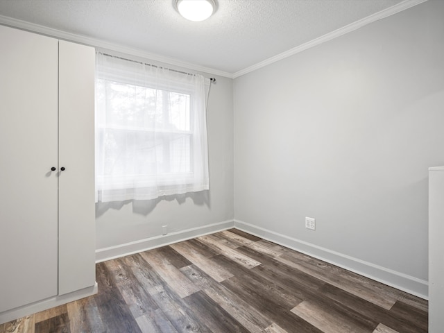 empty room with a textured ceiling, dark wood-type flooring, ornamental molding, and baseboards