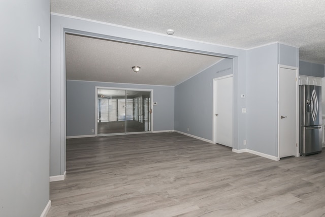 unfurnished living room with a textured ceiling, light wood finished floors, vaulted ceiling, and baseboards