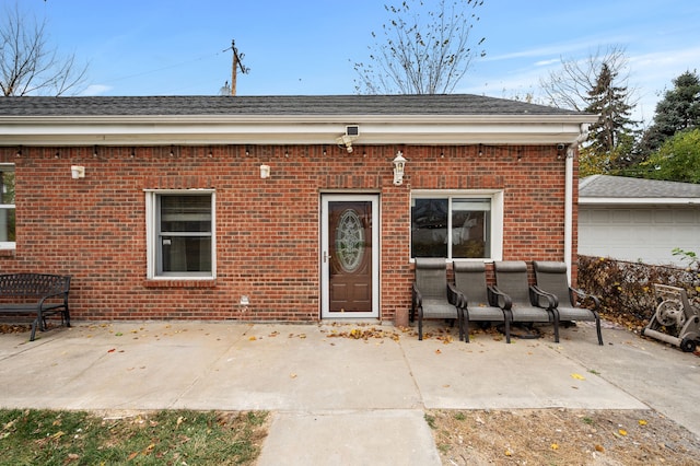 exterior space with a patio area, a shingled roof, and brick siding